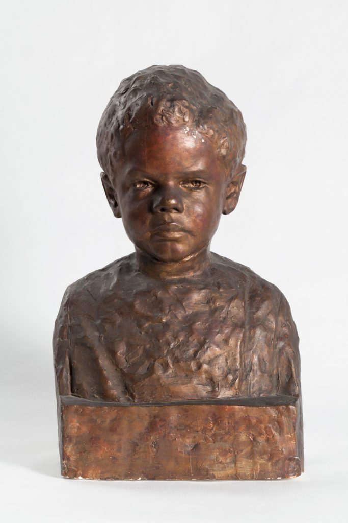 Bronze colored painted plaster bust of a young African American boy with short curly hair and a calm facial expression