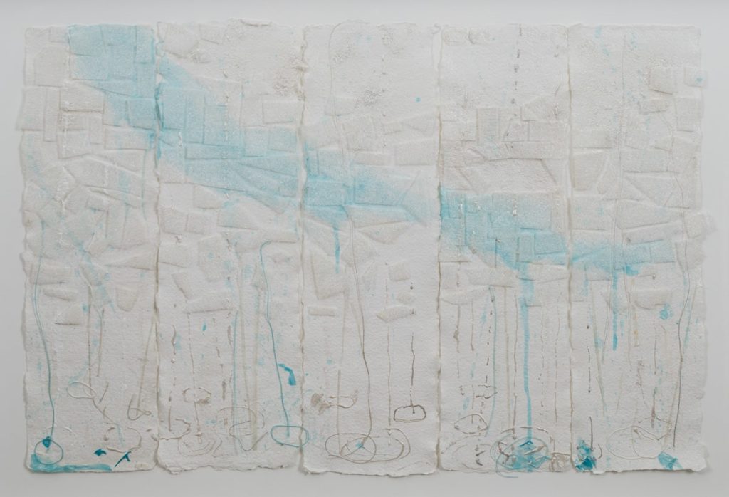 Five strips of white paper, hanging, with drips of light blue, grey, and white paint. Geometric shapes are pasted across the middle of the papers.