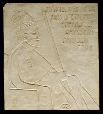 Profile of a man, seated, holding a staff and wearing an ornate hat. Text to the upper right says "Menelik 2 King of the Kings of Ethiopia Emperor of Abyssinia 1864 to 1913"