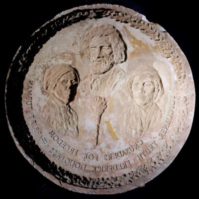 Reverse mold with a laurel wreath boarder containing busts of three African Americans, Sojorner Truth, Frederic Douglas, and Harriet Tubman.