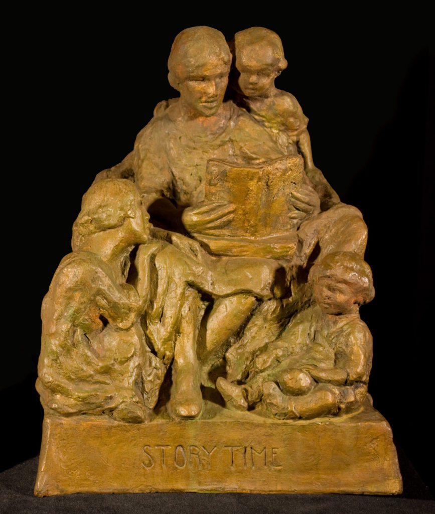 Plaster statuette of three children gathered around a woman, seated reading a book.