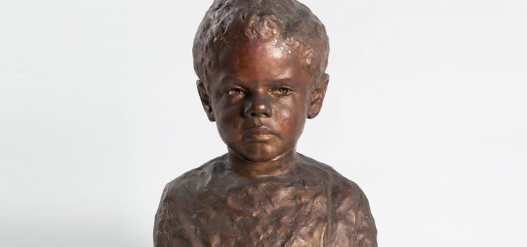 Bronze colored painted plaster bust of a young African American boy with short curly hair and a calm facial expression