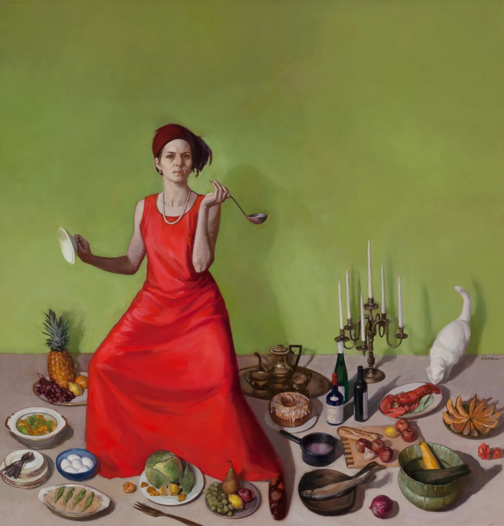 Woman in a red dress standing on a grey table amongst various foods and serve ware with a white cat at the top right corner of the table.
