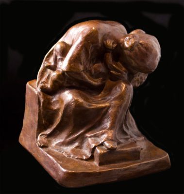 Small sculpture of a mother seated, hunched over, holding a small child barely visible on her lap.