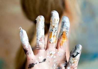 Photograph of a hand with white, yellow, and black paint all over their fingers.