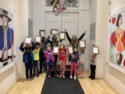 Photograph of a group of kids standing together holding clip boards above their heads, looking excited.