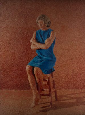 Photograph of a sculpture, with a textured orange wall and floor, and a woman in the same textured orange skin seated on a textured orange stool wearing a blue dress. Her arms are crossed in front of her chest.