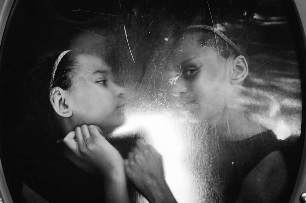 Black and white photograph of two African American girls on the opposite side of a scratched plexiglass circular frame.