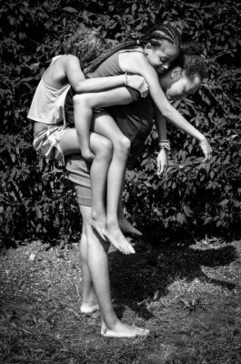 Black and white photograph of three African American girls, the tallest giving a piggyback to two smaller girls.