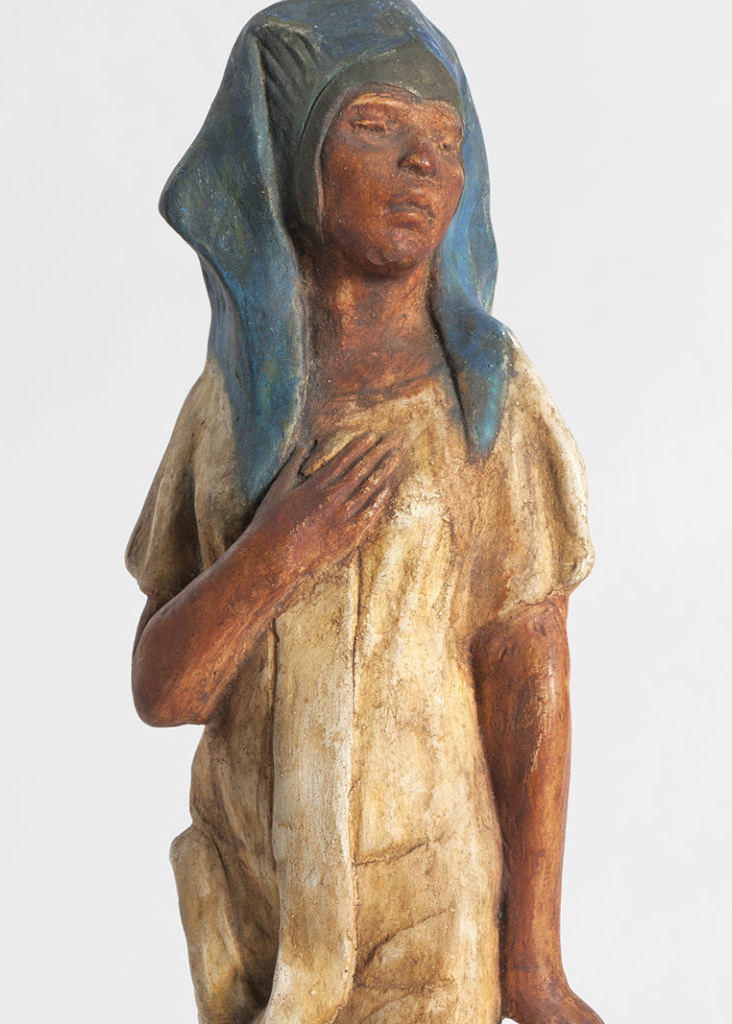 Standing figure of painted plaster with a mummy wrapping dress in tan and a woman emerging from the top with brown skin and a blue head dress.