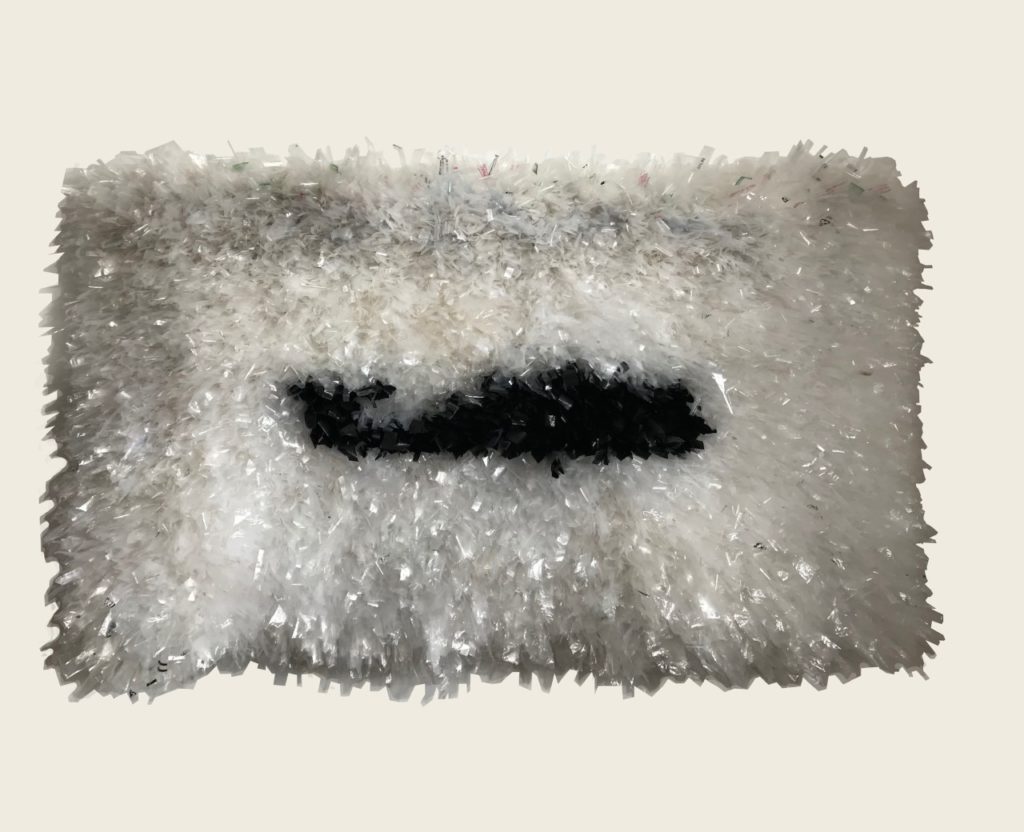 Photograph of a wall hanging shag rug made out of white plastic. In the center is a black whale, facing right.
