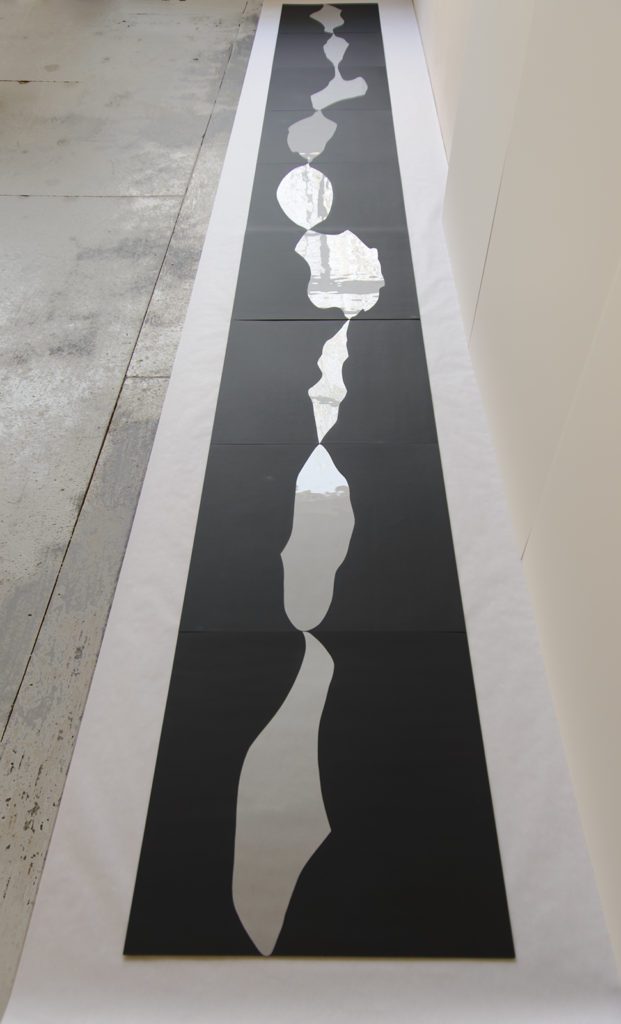 Installation photograph of a floor piece in black, stretching vertically to the top of the photograph, with large connected silver splotches.