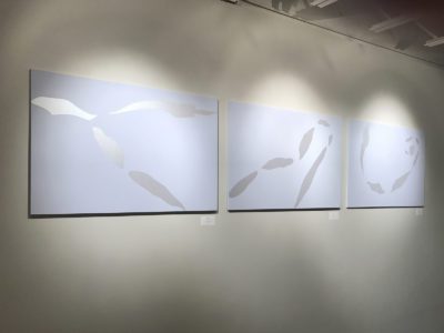 Installation photograph of three blue-purple panels with sliver elongated leaf patterns scattered on each.