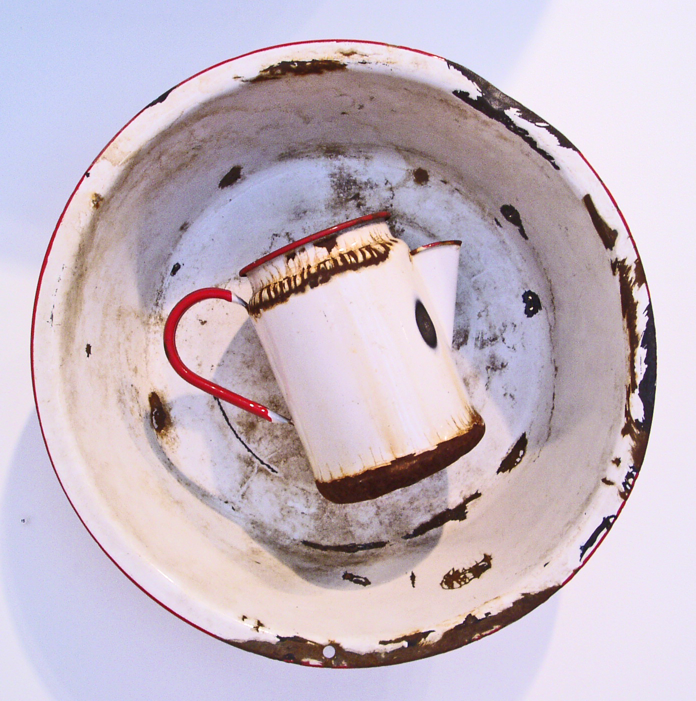 Photograph of a old and rusted white pan an pitcher with red rims.