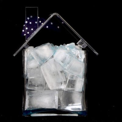 Photograph with a deep black background and a plexi house in the foreground filled with objects. This one is filled with various sized ice cubes and hanging silver stars.
