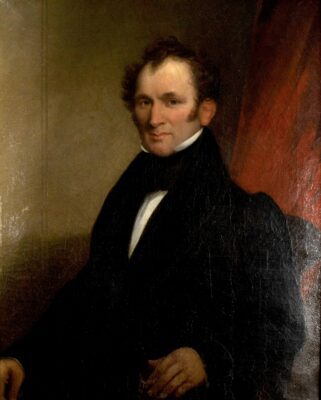 Portrait painting of a man in a 19th century black suit with tall neck. He is seated with a red curtain behind him to the right. He is facing to the left looking out at the audience, with short balding hair.