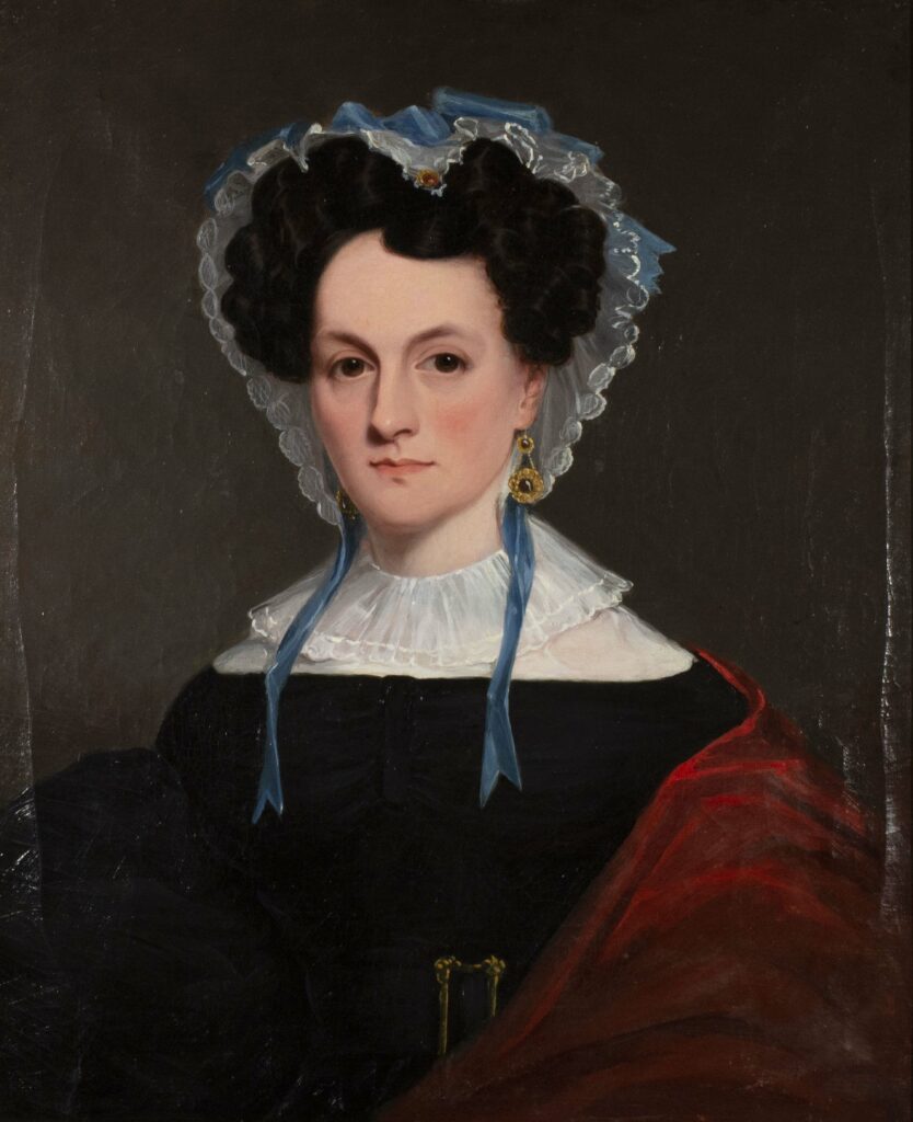 Portrait painting of a woman in 19th century clothing, with a white ruffled neck and lacy bonnet with blue ribbons. Her black hair is pinned up in curls and she has a wide gold belt buckle at her waist and a red shawl around one arm.