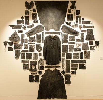Photograph of a wall installation made of black old fabric taken from various clothes. They are laid out roughly in a diamond shape.