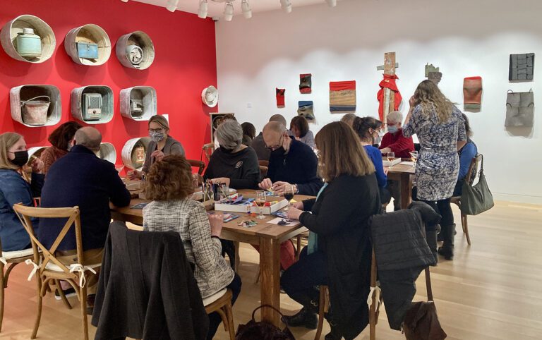 Photograph of a group of people around two long galleries in an exhibition room. They are doing crafts.