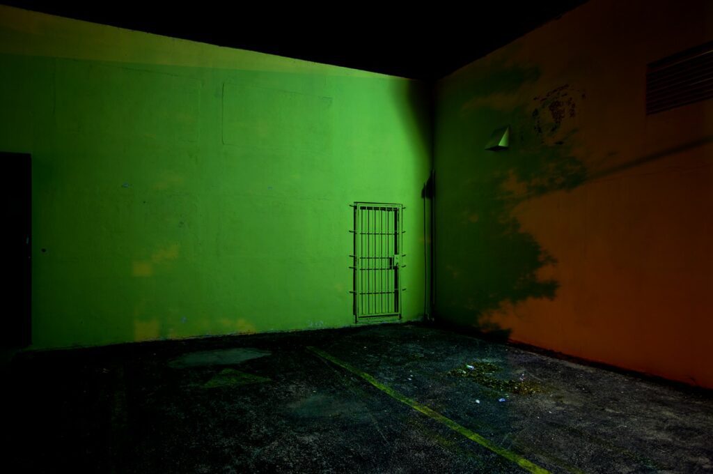 Photograph of a night scene in a parking lot with a corner of a building. The right side is a deep red while the center left wall is a bright green.