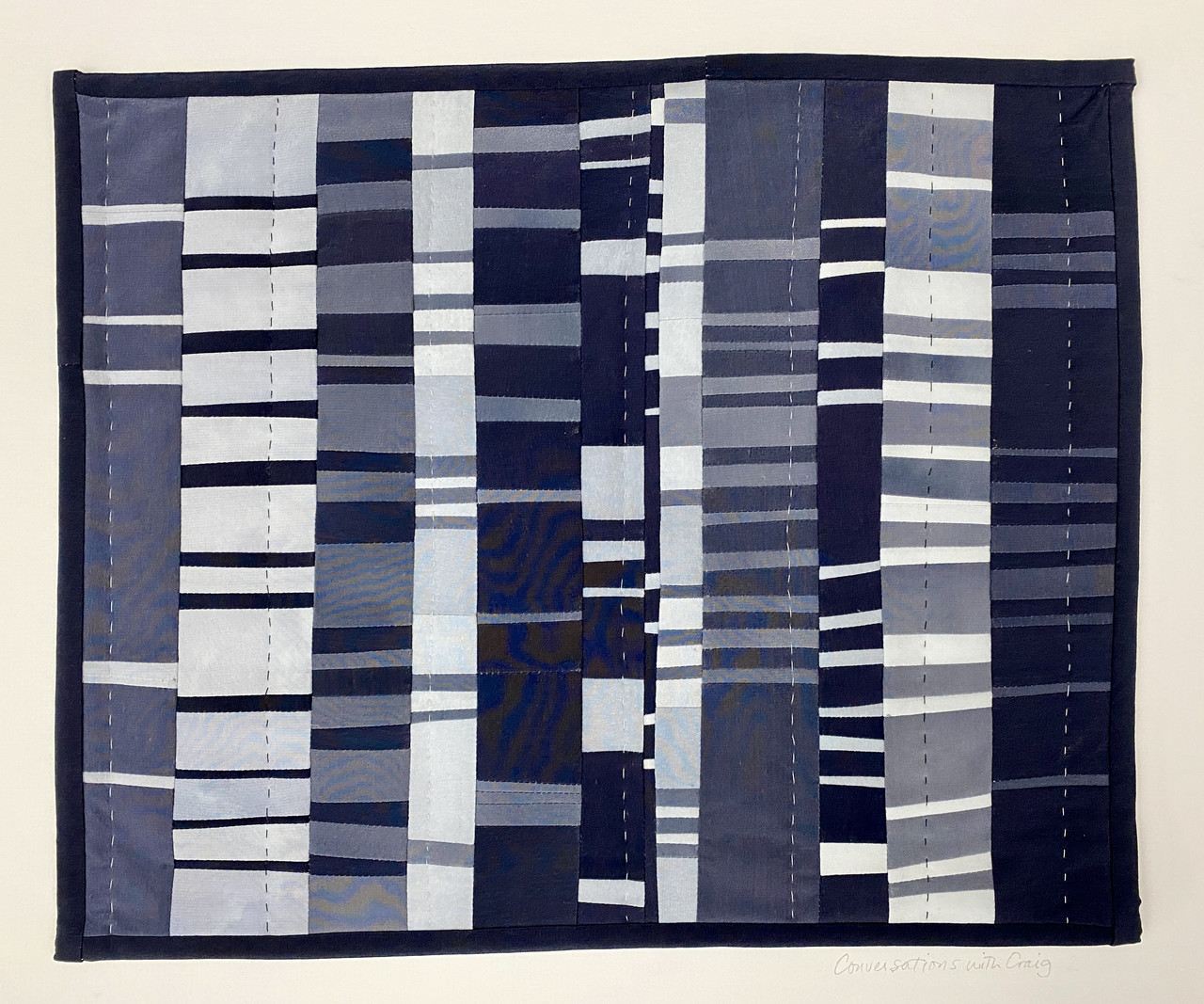 Photograph of a small fabric quilt. The fabric is in hues of black, greys, and white, done in vertical columns with bits of opposite colors in horizontal lines within those columns.