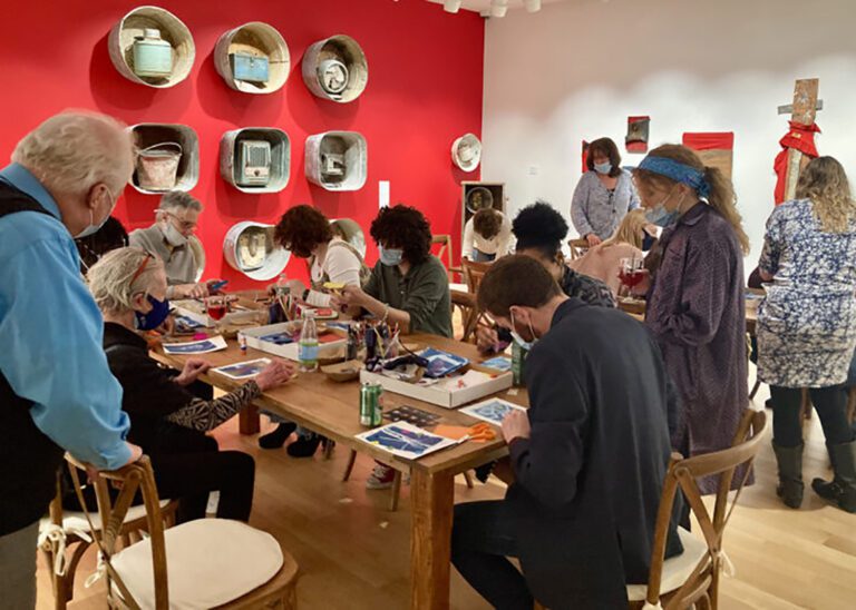Photograph of a group of people around two long galleries in an exhibition room. They are doing crafts.