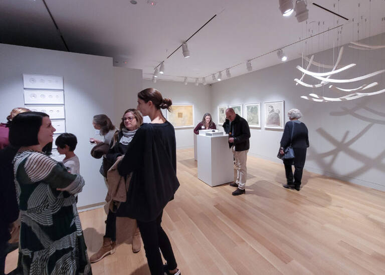 Photograph of a gallery installation with several groups of people enjoying the space.