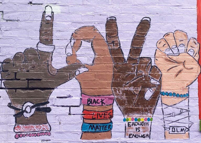 Close up of a mural with a pink background and hands with bracelets signing 'LOVE'.