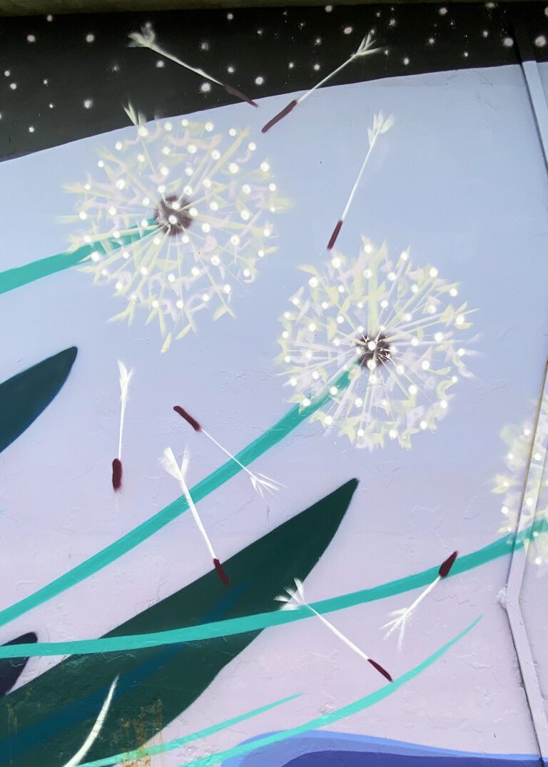 Close up of a mural with a pinky-blue background, lines of green grasses, and two dandelions with seeds blowing away.