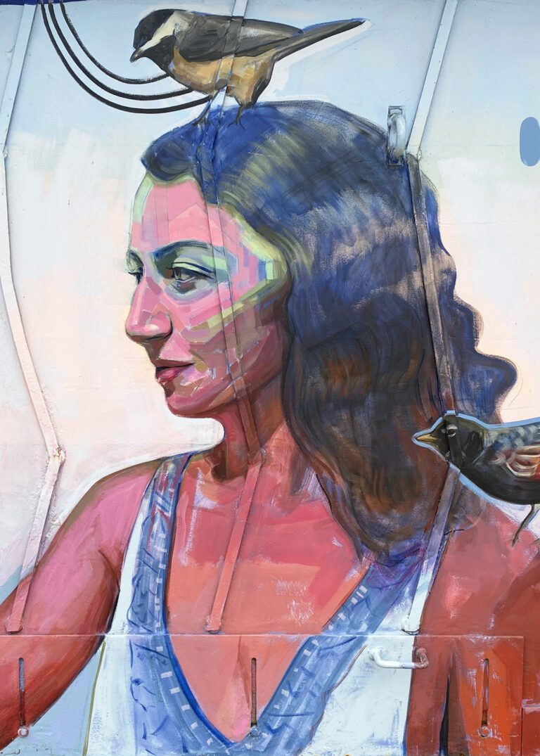 Close up of a mural with a woman from chest up with long wavy hair, facing to the left. She has a blackbird on her right shoulder and a chickadee on her head.
