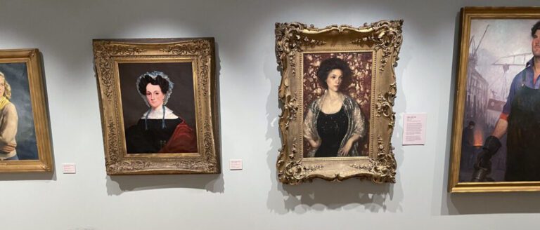 Photograph of four painted portraits hanging on a grey wall.