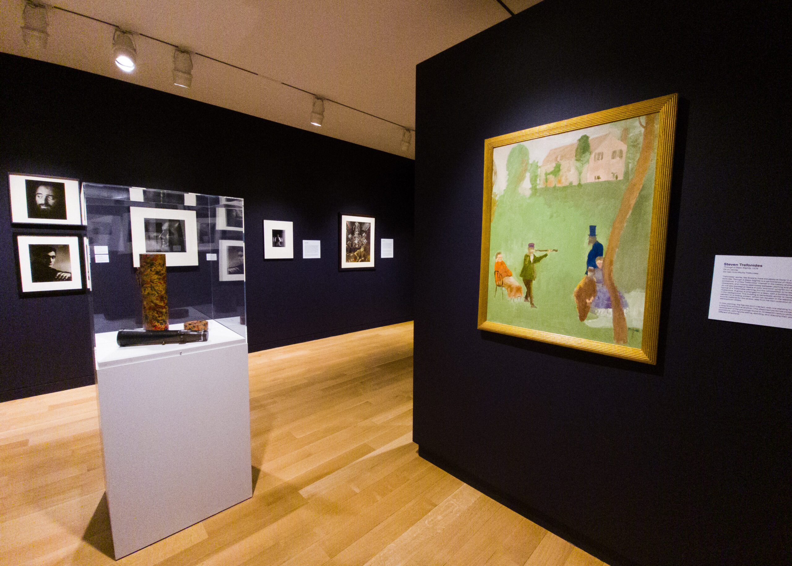 Photograph of a museum gallery room with various paintings and photographs hanging on deep purple walls.