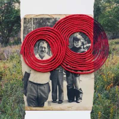 Photograph of an old photograph in the center with the man and young girl's faces encircled by wide red string circles. On either side vertically is a colored photograph of a meadow torn in half bracketing the black and white photo.