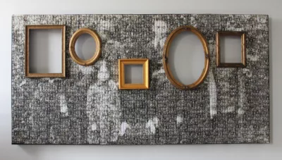 Wall installation with a dotted surface revealing a fuzzy black and white photograph of a family. Cut into the installation a gold picture frames, empty, at various heights and sizes.