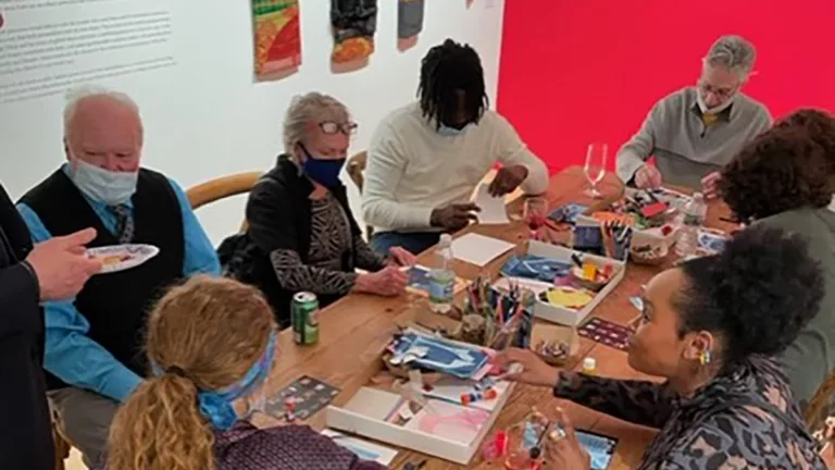 Photograph of a group of people around two long galleries in an exhibition room. They are doing crafts.