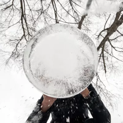 Photograph of an ice ball in the center with reflections of a person and trees around it.
