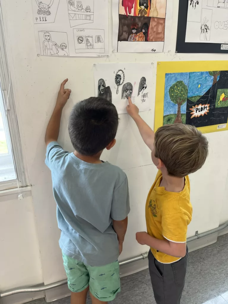 Photograph of two young boys looking at artwork hanging on a white wall.