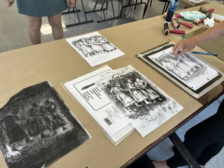 Photograph of a table with charcoal sketches. The sketches show a group of three standing together in crouched shapes.