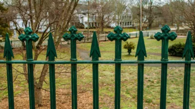 Photograph of a deep green metal fence around a plot of land.