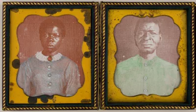 Photograph of two photos inside a small case. The photo on the left is a woman in a blue dress. The photo on the right is a man in a bright green shirt.