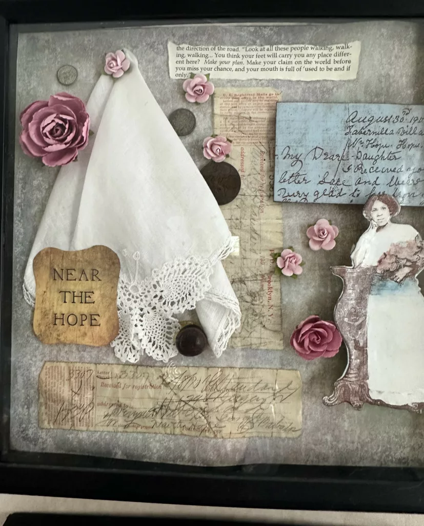 Shadow box with a tan background. Across it are various objects, such as a woman to the bottom right leaning on a pedestal, a white cloth to the top left, and various pieces of paper across the background.