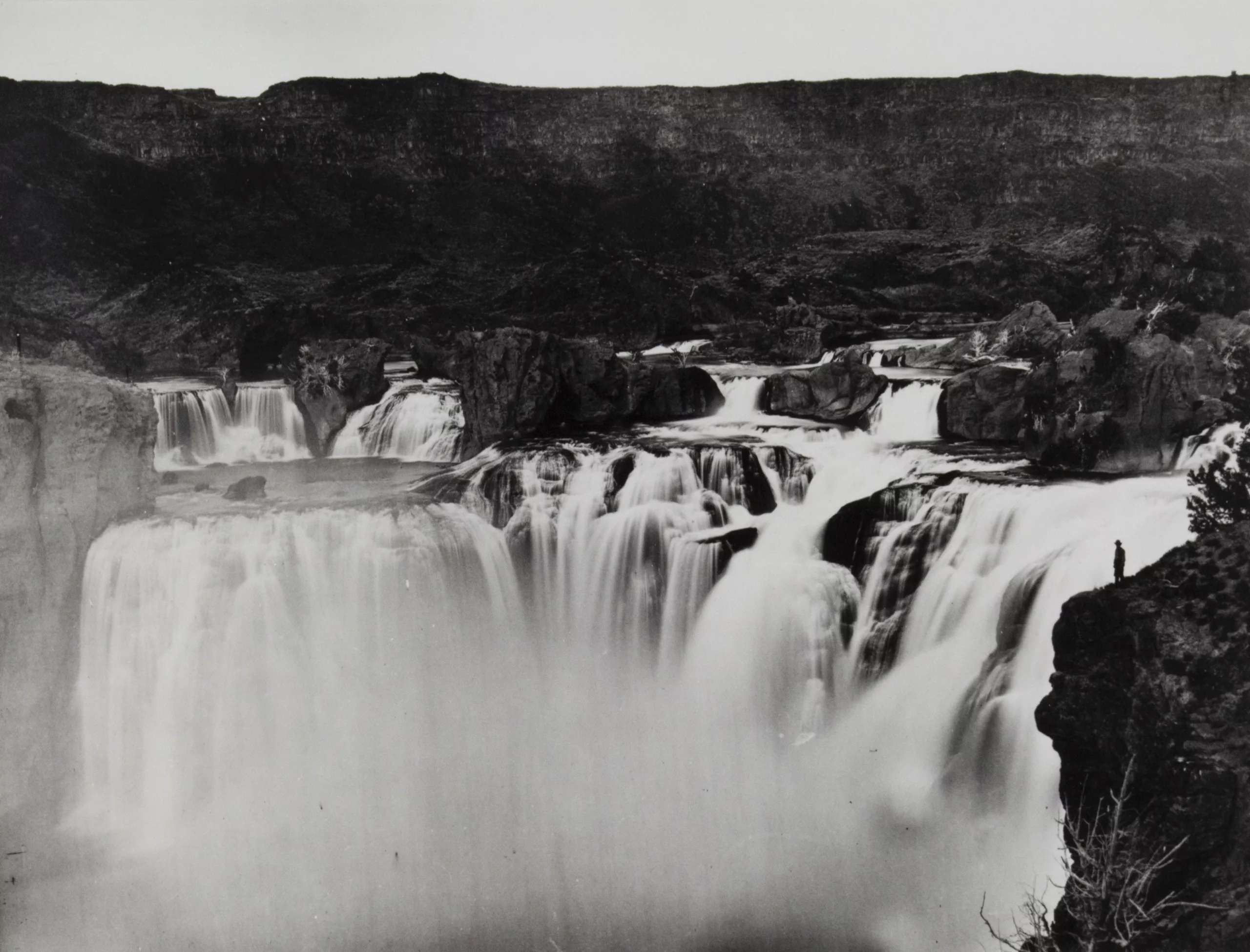 Black and white photograph of a barren landscape, with a stepped waterfall in the center foreground.