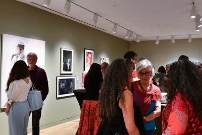 Photograph of a gallery room with sage green walls and people chatting within the room.