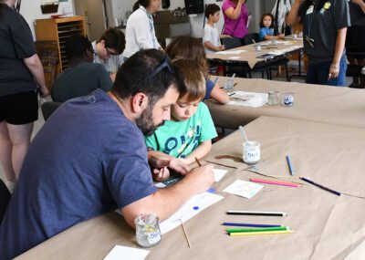 Photograph of a dad and son seated at a brown covered table drawing.