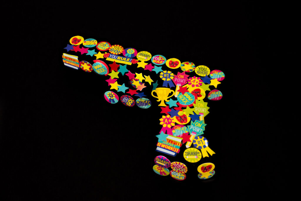 Photograph with an intense black background with a black gun covered in brightly colored stickers.