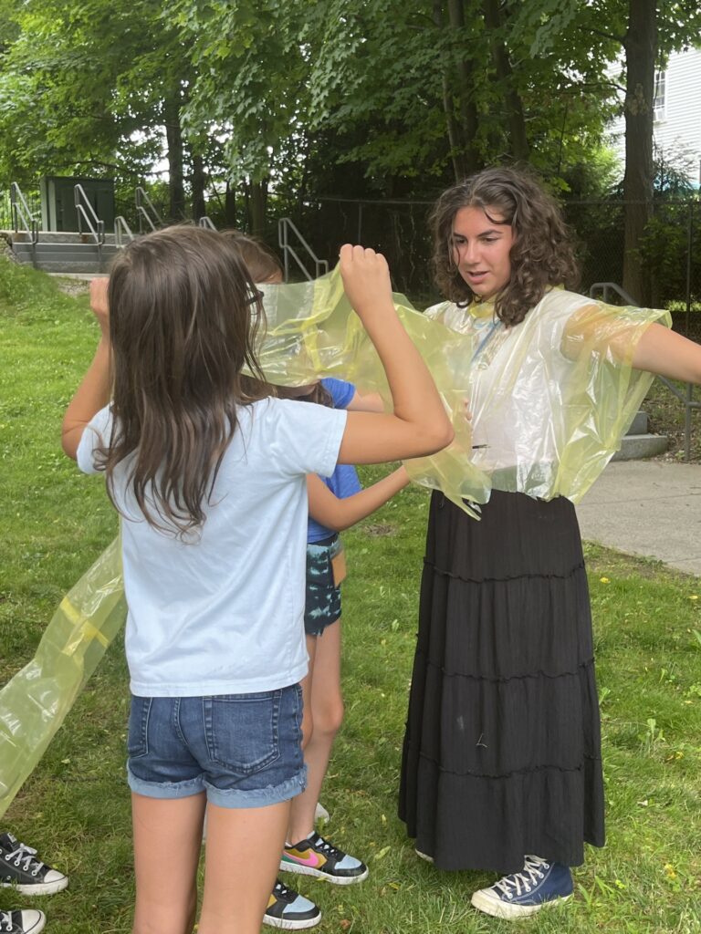 Photograph of a group of students outside holding with yellow bags. The girl on the right is wearing one of the bags around her torso.