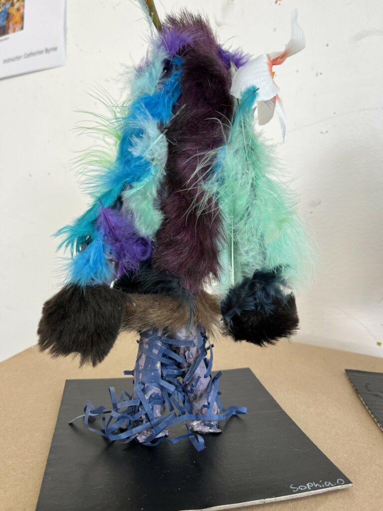 Photograph of a humanoid creature covered in brown and black fur and blue and teal feathers.