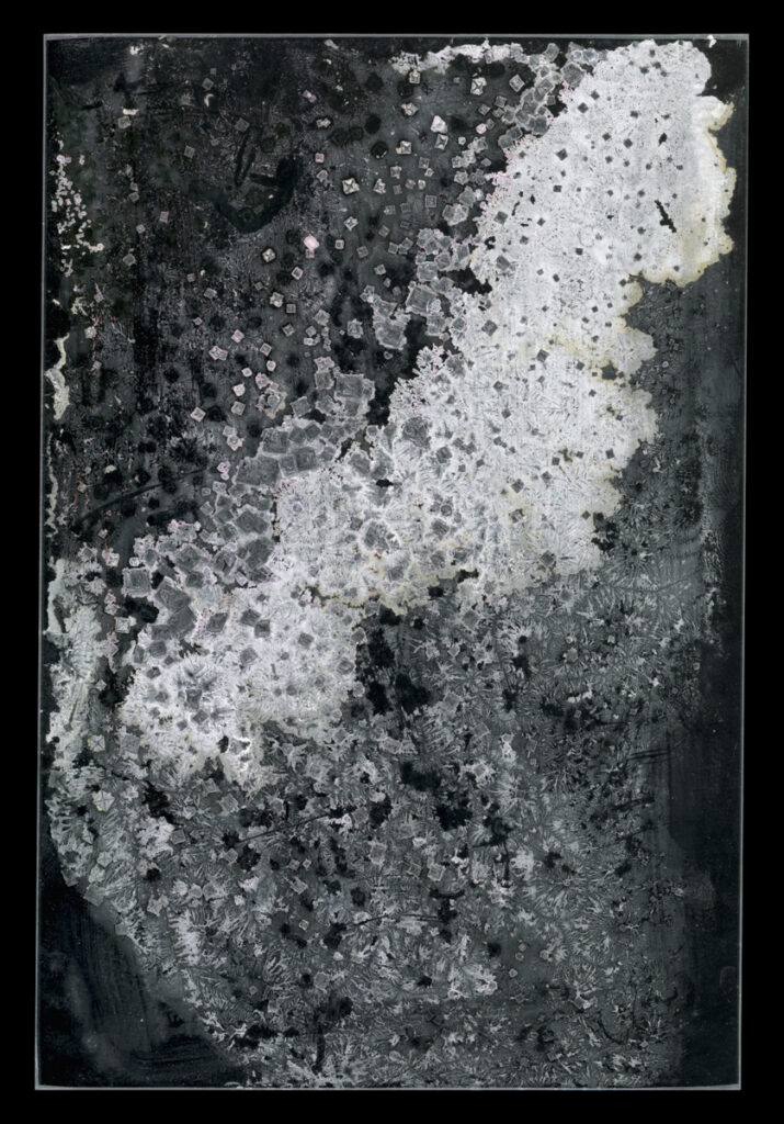 Photograph of crystal and cube shapes on a black background. The crystals are in shades of grey, peach, and white, with white mostly in the center in a diagonal line from bottom left to top right.