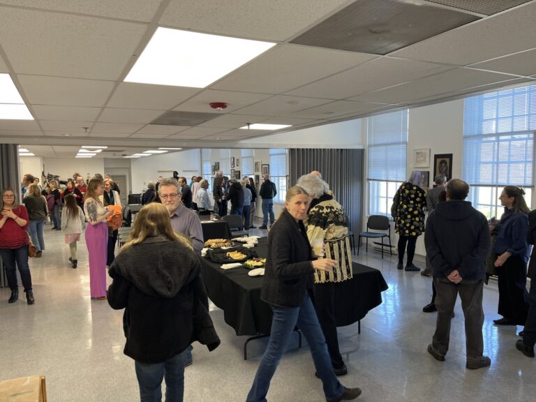 Photograph of a studio set up for a reception. People are milling about, looking at art and chatting.