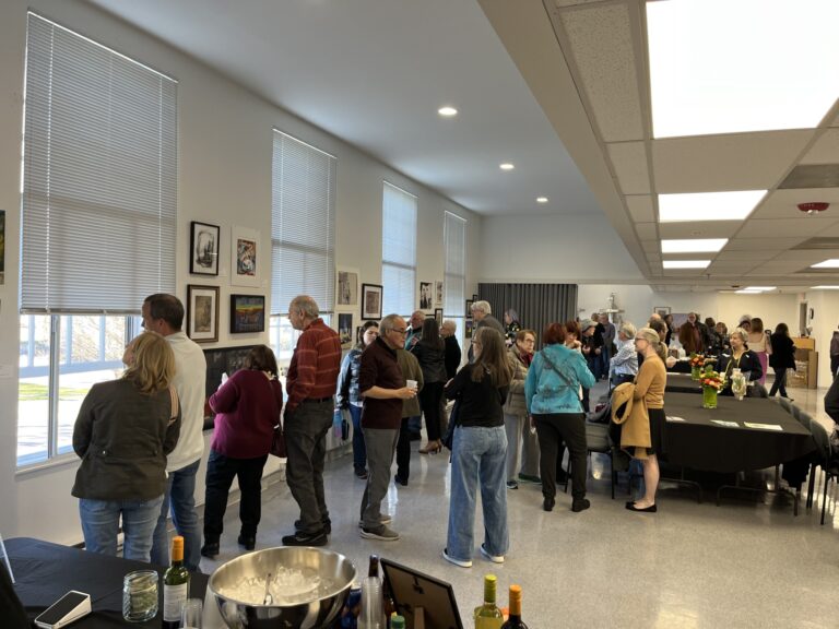 Photograph of a studio set up for a reception. People are milling about, looking at art and chatting.